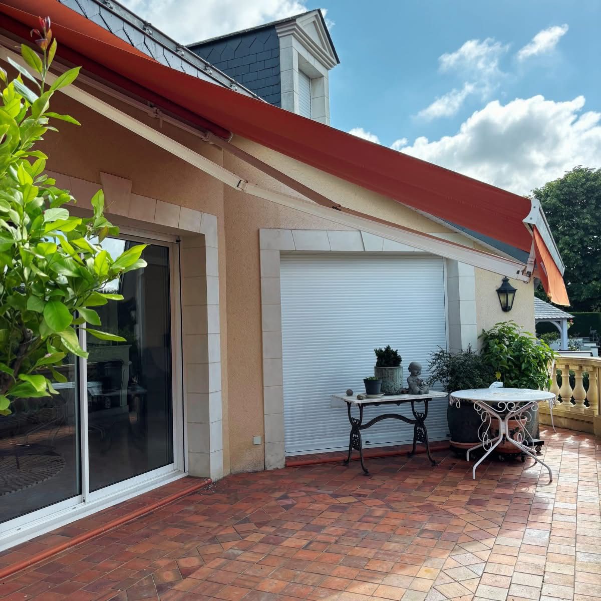 Store banne orange et volet roulant blanc sur une terrasse carrelée